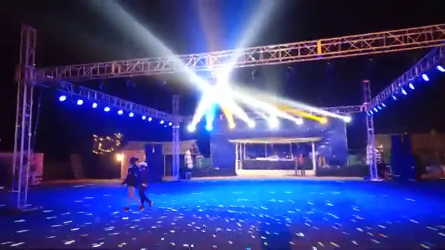 Moving beam lights fanning out from a truss over an open-air dance floor at night