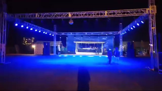 Open-air event ground at night with truss lighting and speaker stacks on both sides of the dance floor